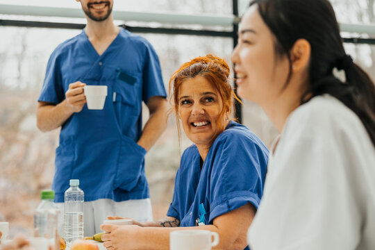 Smiling female medical expert sitting with coworker during break time in hospital cafeteria