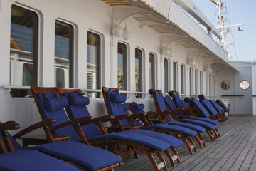 Sun or pool deck with elegant teak wood deck chairs and loungers onboard outdoor patio terrace of...
