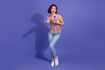 Stylish young woman singing and dancing in a party outfit with microphone on a vibrant purple background