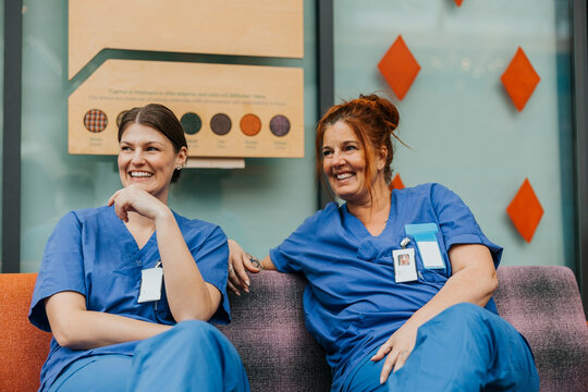 Happy female healthcare experts spending leisure time sitting on sofa in hospital lobby