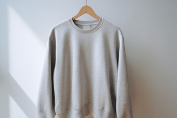 Light gray sweatshirt hanging on wooden hanger in natural sunlight, minimalist casual clothing mockup for branding and fashion presentation
