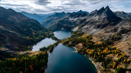 Aerial view of autumn lakes surrounded by orange forsts and rugged mountain peks.