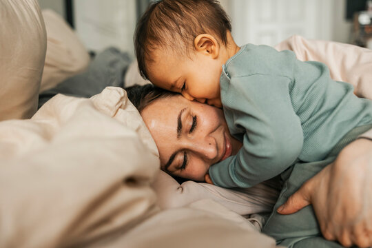 Cute baby boy with mother on bed at home