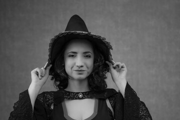 Black and white portrait of a beautiful witch holding her hat with both hands on her head. Suitable for Halloween, witchcraft and fantasy fairy tale. Horizontal studio portrait with copy space.