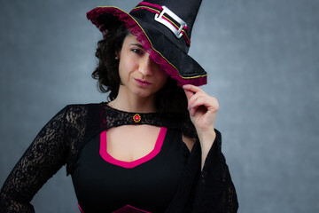Beautiful witch in black and pink costume, hiding one eye with her hat. Ideal for Halloween, mystery, witchcraft and fairy tale. Horizontal studio portrait with copy space.