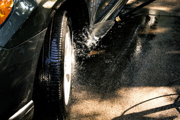 a dark-colored car being washed with a focus on the front tire and lower body panel. A...