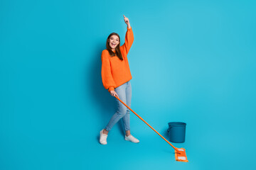 Happy young woman enjoying house cleaning with a mop wearing cozy casual orange sweater on bright...