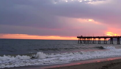 Fototapeta premium A dramatic sunset paints the sky in hues of pink and orange over a peaceful beach scene with a pier stretching into the ocean.