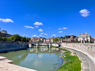 Historische Br&uuml;cke &uuml;ber den Tiber in Rom bei blauem Himmel.
Beschreibung: Malerischer Blick auf den Tiber in Rom mit historischer Br&uuml;cke, alten Geb&auml;uden und klarem Sommerhimmel.