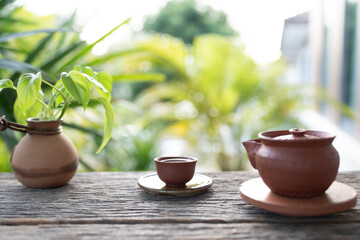 brown earthenware tea set placed on a rustic wooden table with lush green background