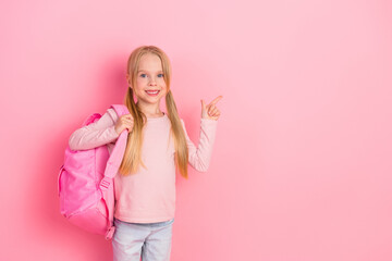 Adorable young girl showcasing a cheerful pose with a pink backpack against a vibrant background,...