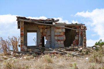 A crumbling brick structure stands abandoned in a dry field, surrounded by scattered debris and...