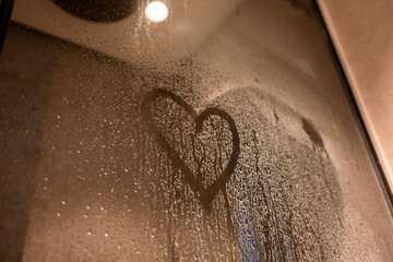 A heart is drawn on a window with water droplets on it. Concept of intimacy and warmth