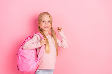 Adorable young girl with pink backpack smiling joyfully wearing pastel clothing standing against a...