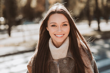 Beautiful young woman enjoying a sunny autumn day outdoors in a park, expressing joy and elegance...