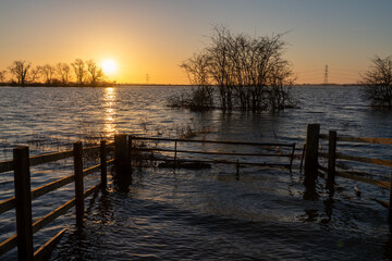 Obraz premium Rising floodwaters covering farmland with submerged fences and trees