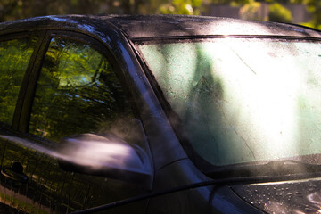 a car being washed or rinsed with motion of water mist around the side mirror and windshield. bokeh light effect. lifestyles design element or background.