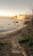 Man standing on coastal path overlooking beach and historic walls at sunset