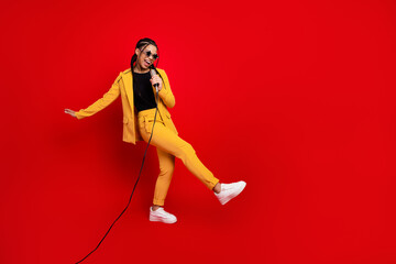 Young woman in a vibrant yellow suit singing into a microphone against a red background, portraying fun and confidence