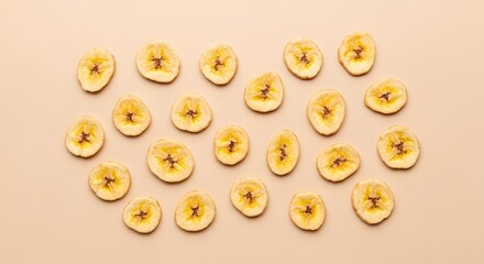 Fototapeta premium Golden Dried Banana Slices Arranged Flat Lay on Light Beige Background as Healthy Snack Food Concept