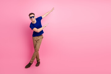 Young man wearing blue t-shirt and sunglass posing against pink background with cheerful gesture,...