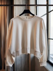 Studio shot of a cream colored sweatshirt hanging on a rack against a window in natural light fashion lifestyle