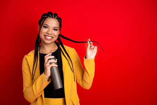 Young woman with stylish cornrow hairstyle in yellow suit smiling gracefully on red background holding a cylindrical object