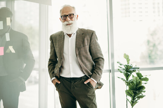 Confident mature businessman with white beard in formal attire posing in modern office environment during work