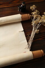 Old rolled scroll, dry flowers and inkwell on wooden table, above view