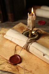 Old rolled paper scroll, sheets and burning candle on wooden table, closeup