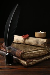 Old rolled scroll, burning candle, feather, inkwell and books on wooden table, closeup