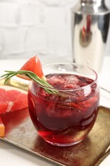 Tasty cocktail with grapefruit, ice cubes, rosemary and shaker on white table, closeup