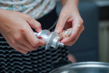 Hands preparing meat by using a grinder in a kitchen during afternoon cooking session
