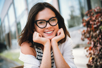 Young woman with stylish glasses smiling in the city on a sunny day, enjoying outdoor leisure and...