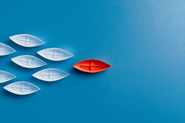 A red boat and a group of white boats on a blue background like the sea. Leadership concept.