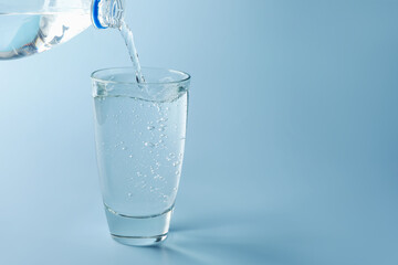 Pouring refreshing soda water from bottle into glass on light blue gradient background, closeup. Space for text