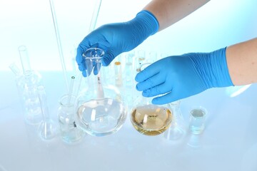 Scientist with flask of dirty water at table against light background, closeup