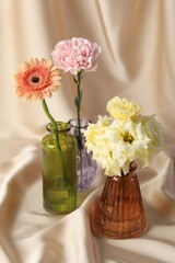 Beautiful flowers in glass vases on beige cloth, closeup