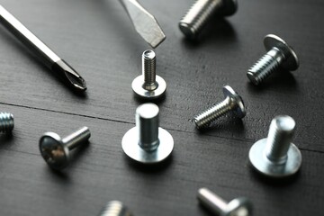 Many metal screwdrivers and bolts on black wooden table, closeup
