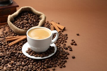 Cup of hot coffee, beans and cinnamon on brown background, space for text