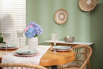 Stylish setting with plates and vase of flowers on wooden table in dining room. Interior design