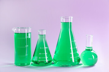 Laboratory glassware with green liquid on lilac background