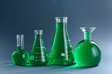 Laboratory glassware with green liquid on grey background