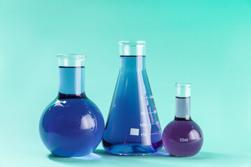 Laboratory glassware with colorful liquids on turquoise background