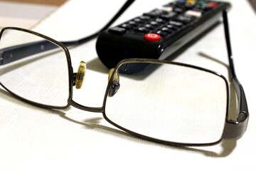 glasses and remote control. Prescription glasses are lying on a white table surface against the background of a TV remote control 