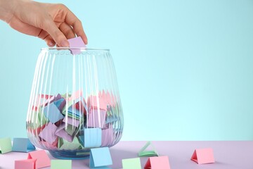 Woman taking violet paper piece from glass jar on color background, closeup. Space for text