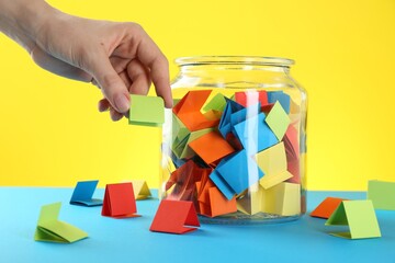 Woman taking green paper piece from glass jar on color background, closeup