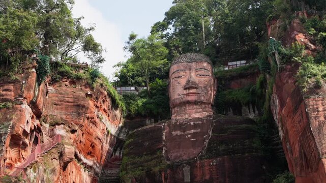 Detailed slow motion view of full Leshan Buddha carved in red sandstone with textures of surrounding natural cliff face