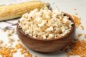 Tasty popcorn and corn kernels on white table, closeup