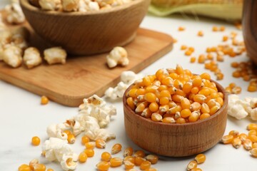 Corn kernels and tasty popcorn on white table, closeup